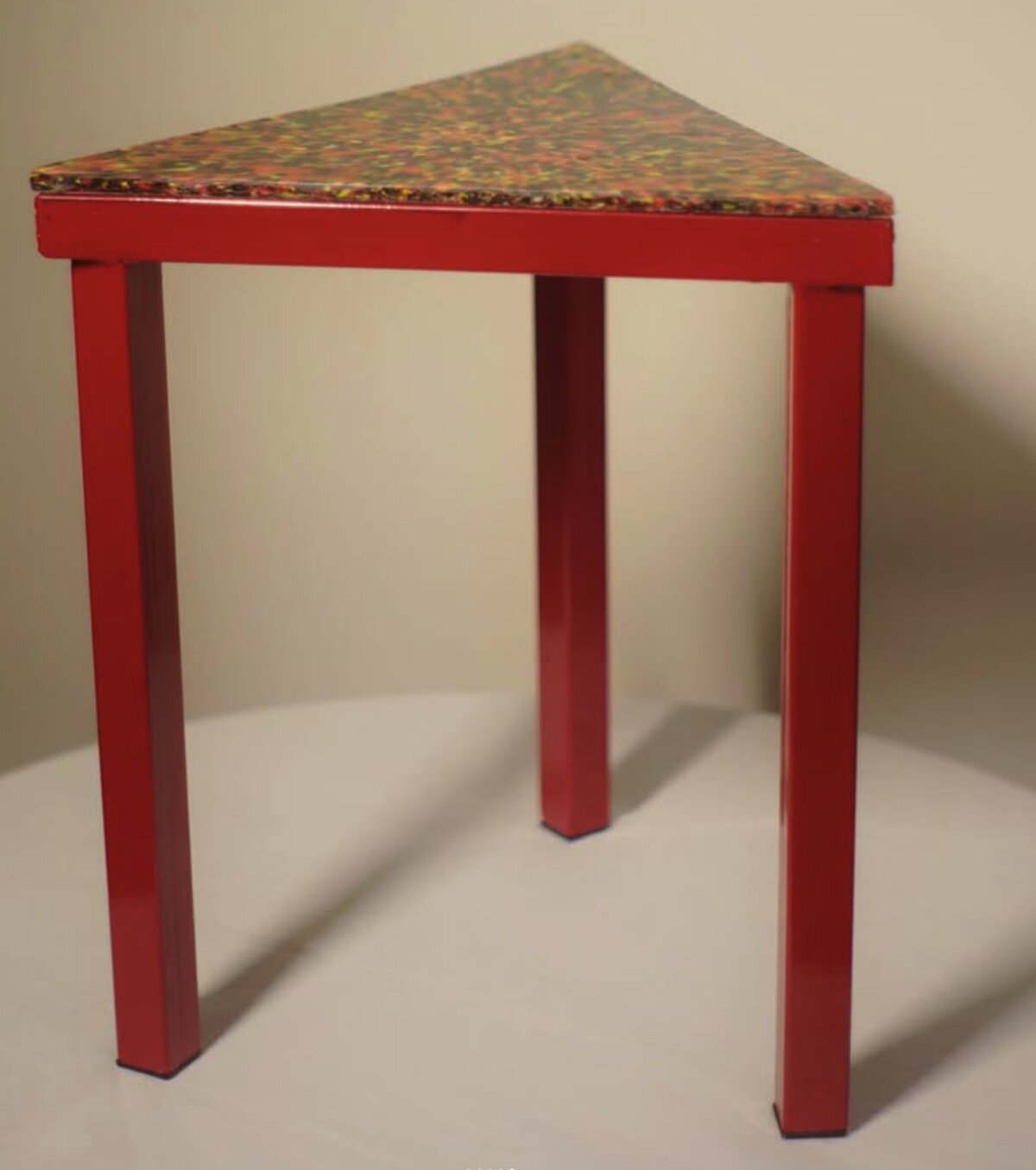 Triangular stool with recycled-plastic speckled top and red steel legs